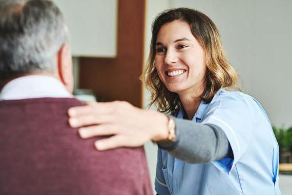 a smiling woman sitting across from a man places her hand his shoulder